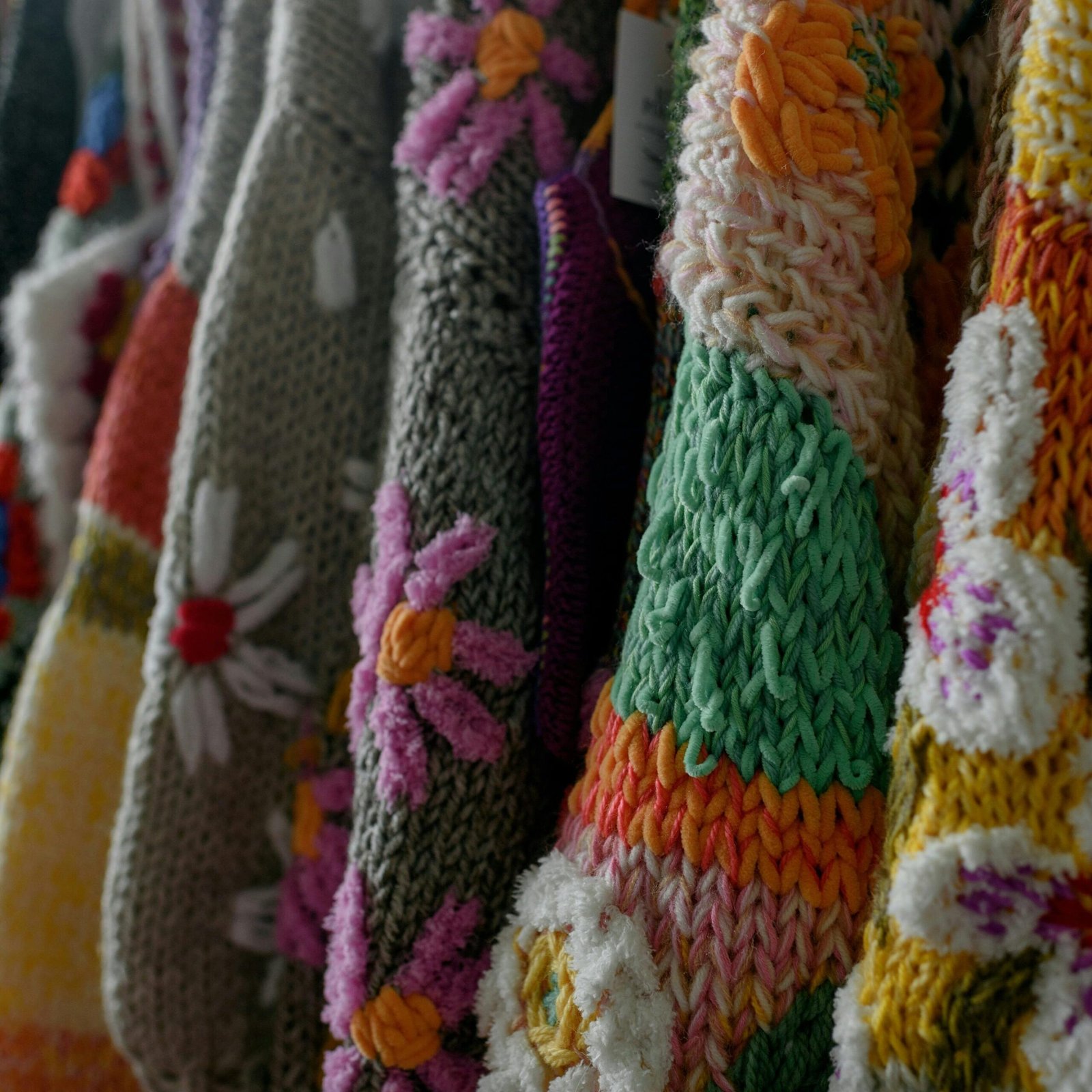 pexels-photo-15170519-15170519 Close-up view of vibrant handmade knitted sweaters with floral patterns.