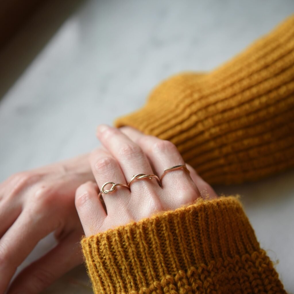 pexels-photo-30720973-30720973 Close-up of elegant minimalist gold rings on hands with a cozy mustard sweater.